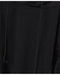Close-up of the front of the black hoodie, with the drawcord, the layered sleeve panel and the angled seam