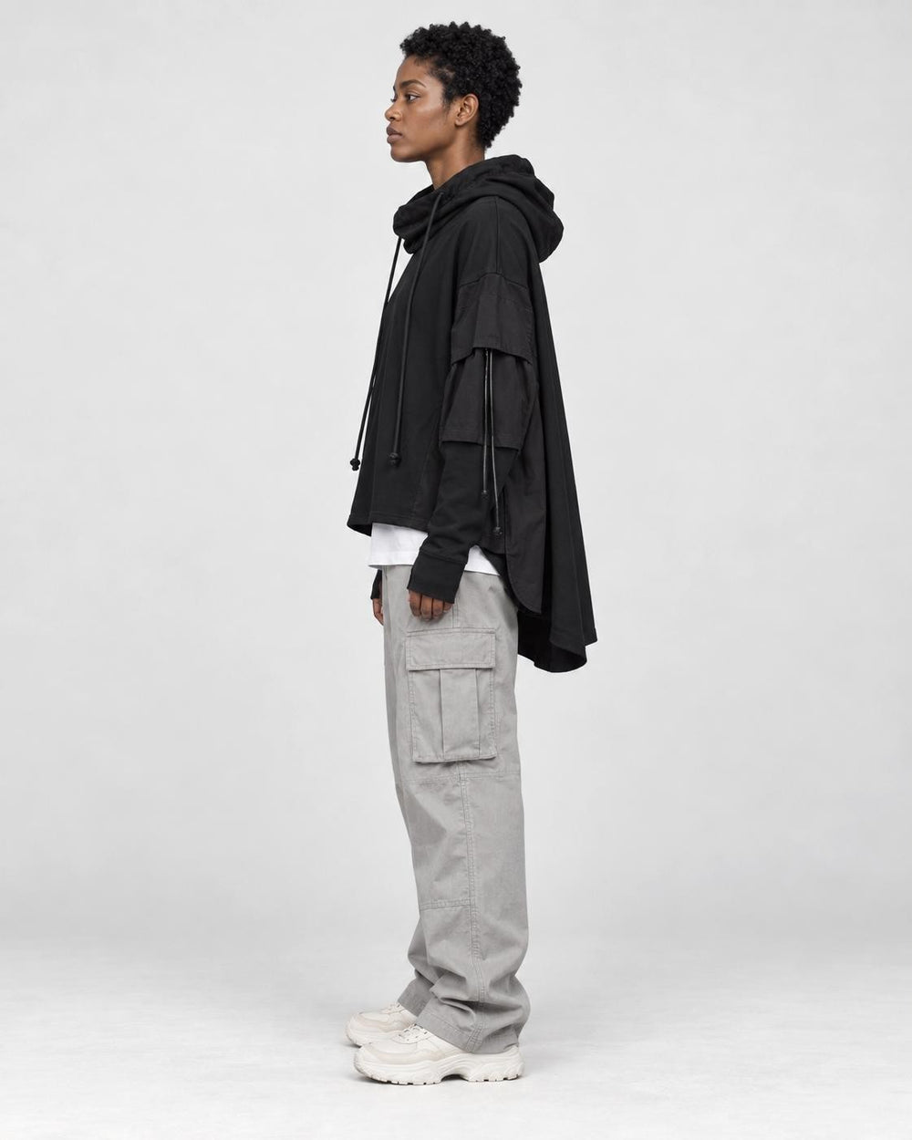Model wearing the black layered sleeve hoodie in profile, showing the long cape panel at the back