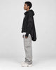 Model wearing the black layered sleeve hoodie in profile, showing the long cape panel at the back