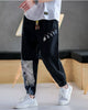 Black linen-cotton jogger pants with buttoned tabs on the thigh and an ink-wash print panel on the lower leg