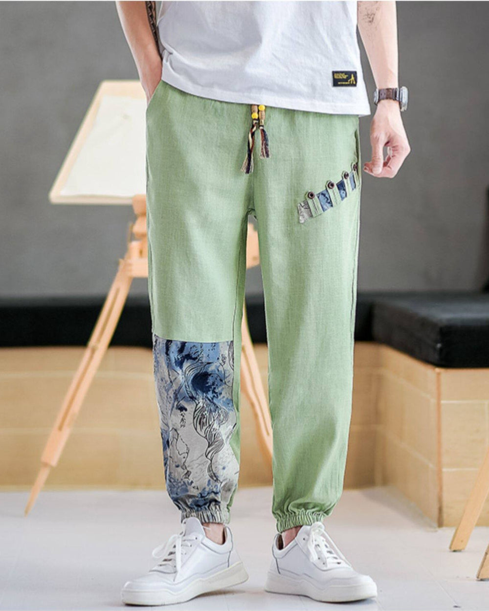 Light green linen-cotton jogger pants with buttoned tabs on the thigh and an ink-wash print panel on the lower leg