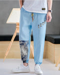 Sky blue linen-cotton jogger pants with buttoned tabs on the thigh and an ink-wash print panel on the lower leg