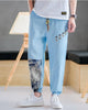 Sky blue linen-cotton jogger pants with buttoned tabs on the thigh and an ink-wash print panel on the lower leg