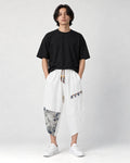 Model wearing the white linen drop-crotch pants with a black tee and white sneakers, front view