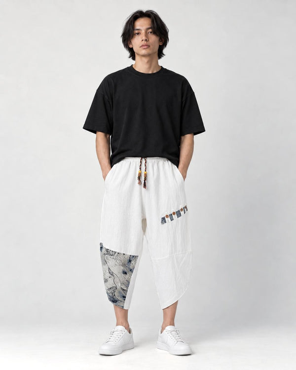 Model wearing the white linen drop-crotch pants with a black tee and white sneakers, front view