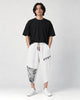 Model wearing the white linen drop-crotch pants with a black tee and white sneakers, front view