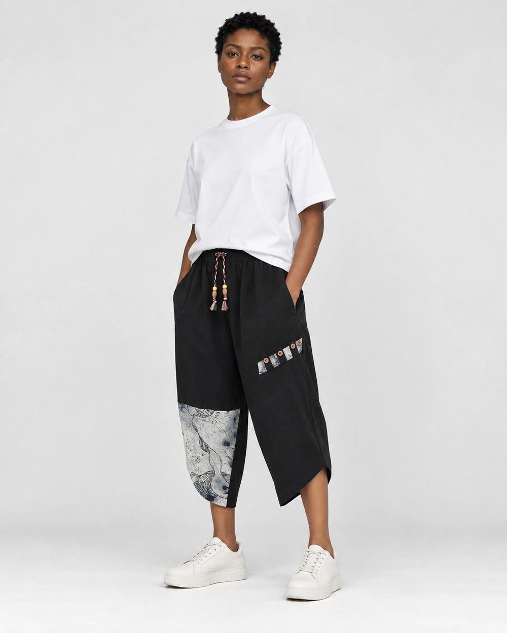Model wearing the black linen drop-crotch pants with a white tee and white sneakers, three-quarter view