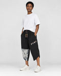 Model wearing the black linen drop-crotch pants with a white tee and white sneakers, three-quarter view
