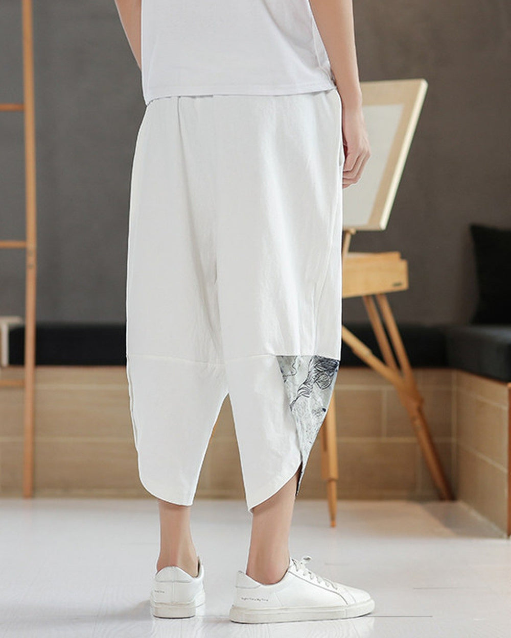 Back view of the white linen pants showing the slanted hem and the printed panel on the lower leg