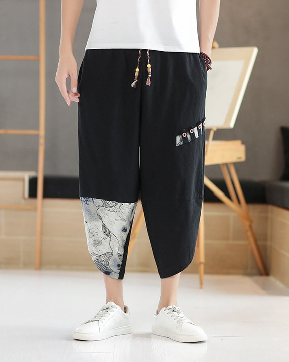 Black linen drop-crotch pants with a toggle patch row on the thigh and an ink-wash print panel on the lower leg