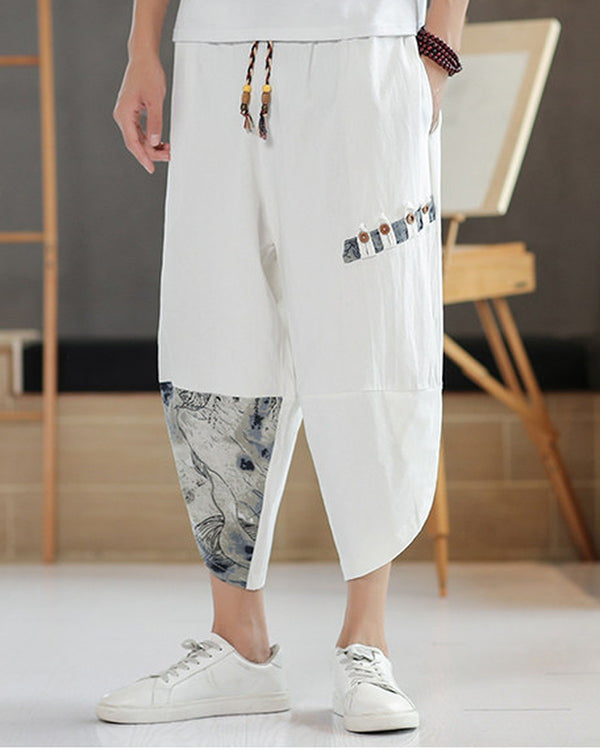 White linen drop-crotch pants with a toggle patch row on the thigh and an ink-wash print panel on the lower leg