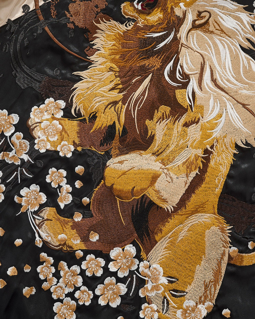 Close-up of the embroidered lion with its cream mane among blossoms