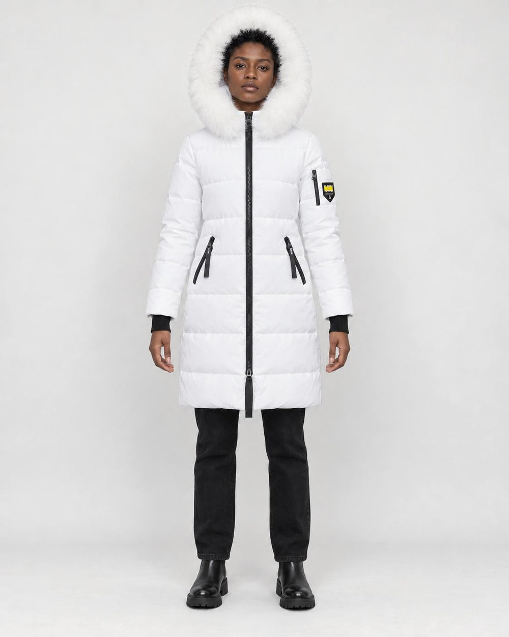 Model wearing the white long puffer coat with a white faux-fur hood, black jeans and black boots, front view