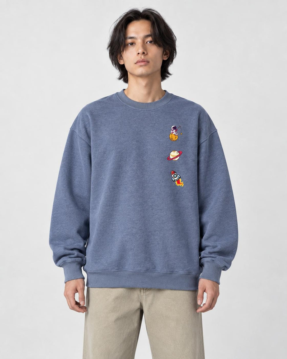 Model wearing the dusty blue crewneck sweatshirt with three small space icons on the chest, with stone trousers