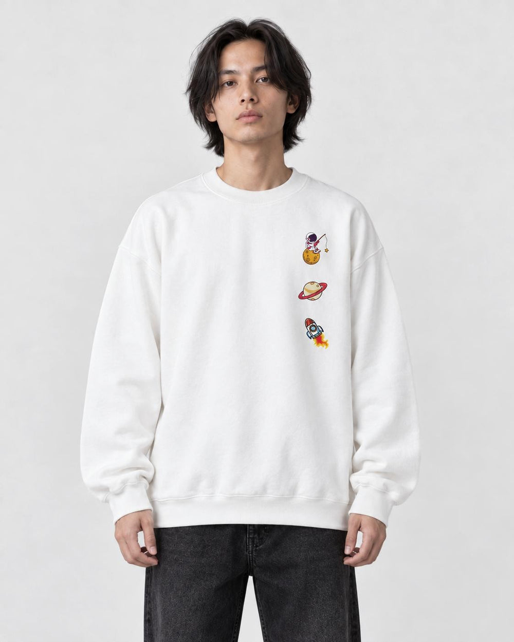 Model wearing the white crewneck sweatshirt with three small space icons on the chest, with black jeans, front view