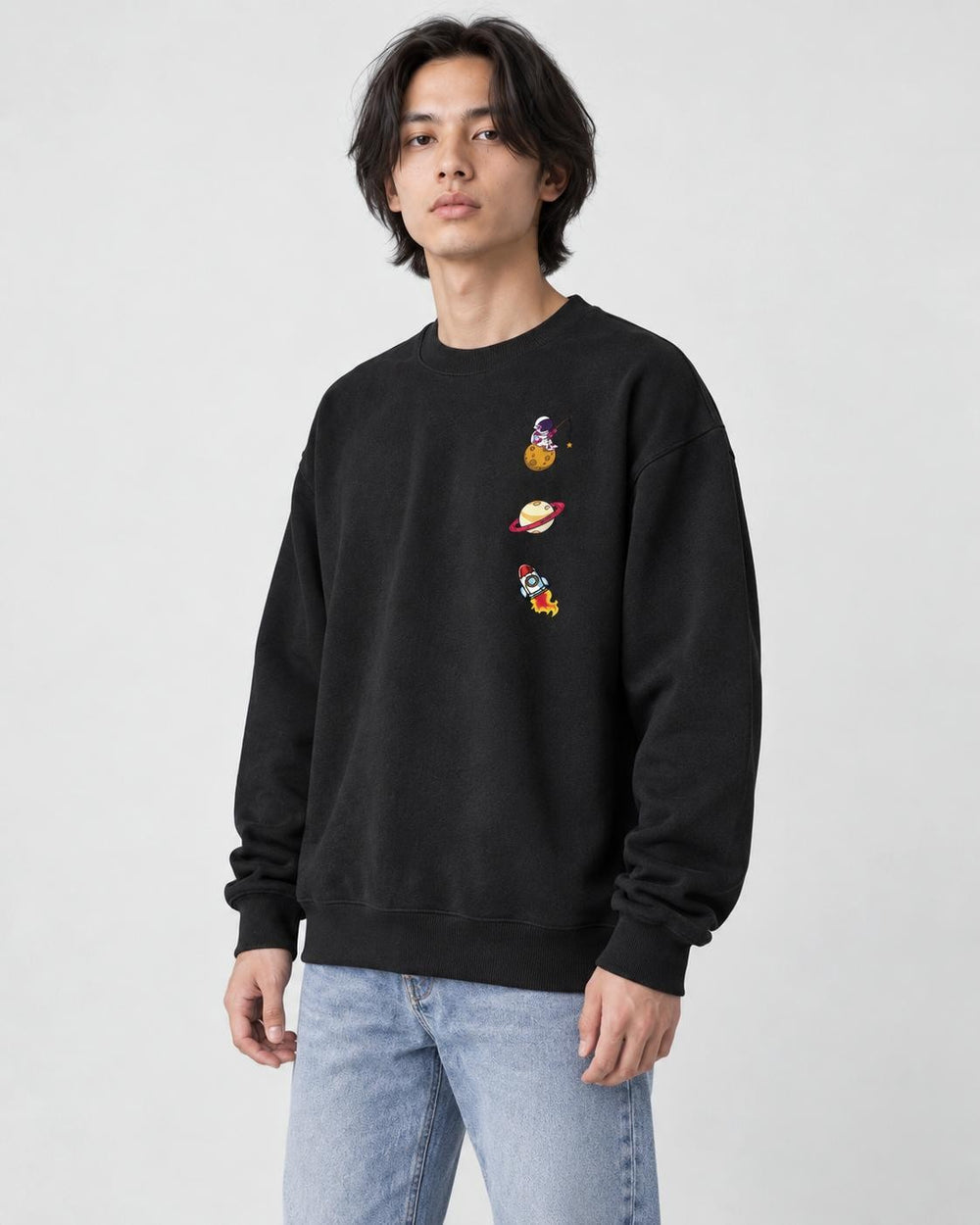 Model wearing the black crewneck sweatshirt with three small space icons, with light-wash jeans, three-quarter view