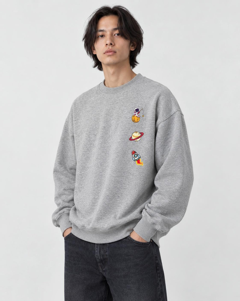 Model wearing the heather gray crewneck sweatshirt with three small space icons on the chest, with dark jeans
