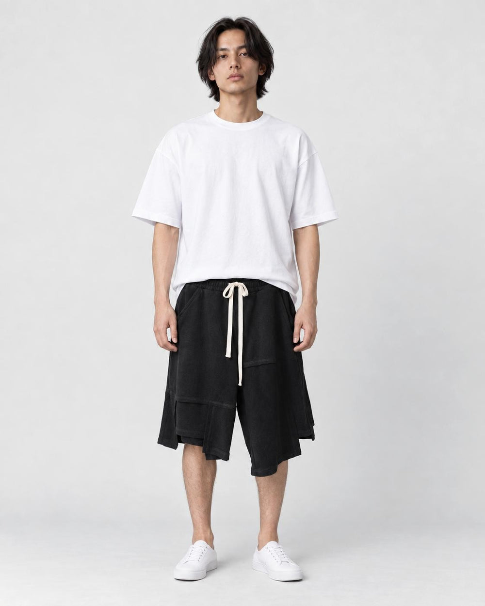 Man in black asymmetric knee-length shorts with an uneven hem, white tee and white sneakers