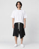 Man in black asymmetric knee-length shorts with an uneven hem, white tee and white sneakers