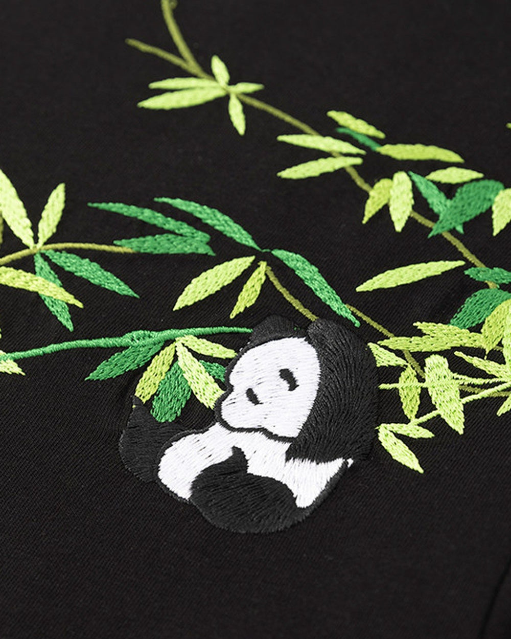 Close-up of the panda curled among green bamboo leaves embroidered on the black T-shirt