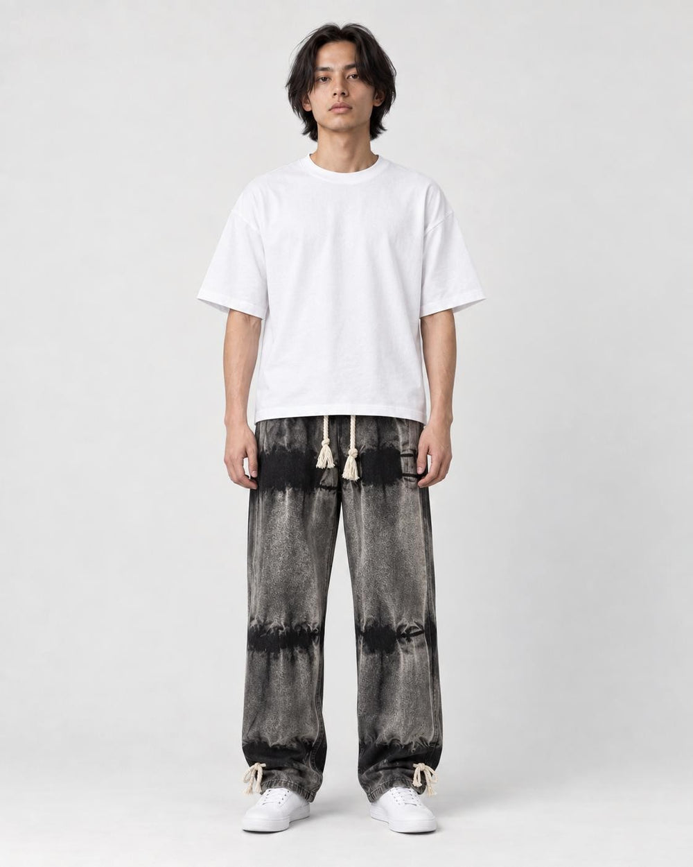 Man in banded charcoal tie-dye straight jeans with a white tee and white sneakers, full length