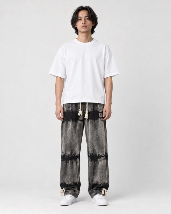 Man in banded charcoal tie-dye straight jeans with a white tee and white sneakers, full length