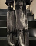 Banded charcoal tie-dye jeans with a cream rope drawcord and ankle cords, worn standing on stairs