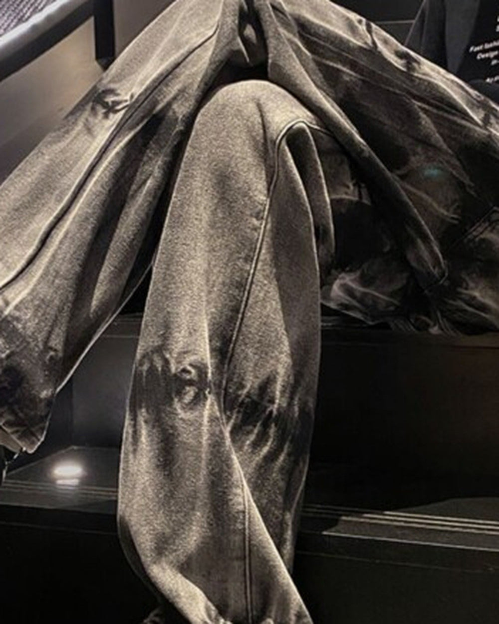 Seated view of the tie-dye jeans showing the washed bands and the rope cord at the ankle
