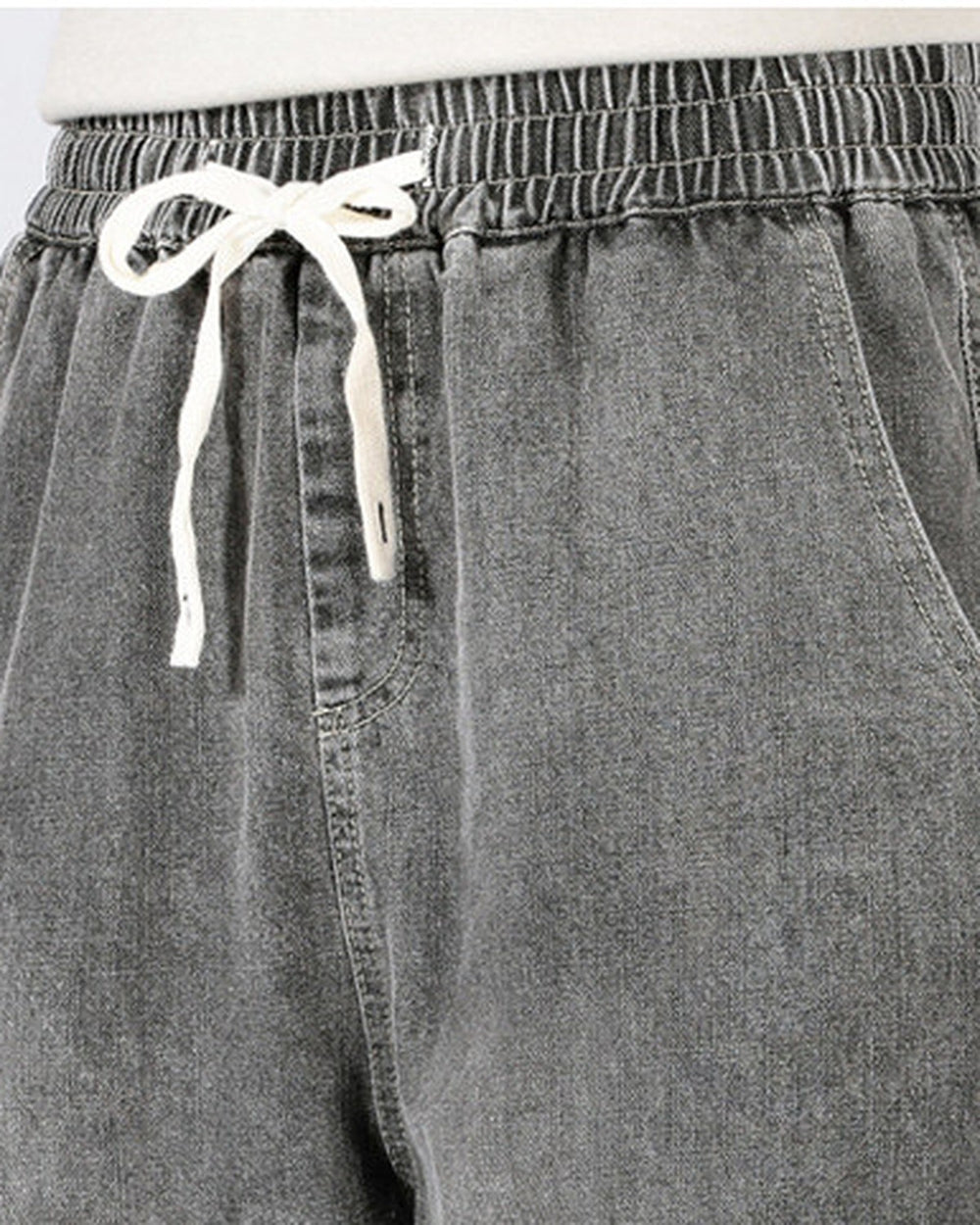 Close-up of the elastic waistband and cream drawcord bow on the washed gray denim joggers