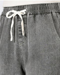 Close-up of the elastic waistband and cream drawcord bow on the washed gray denim joggers