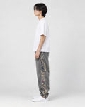 Model seen from the side in the washed gray denim joggers and white sneakers, showing the bear panel on the outer leg