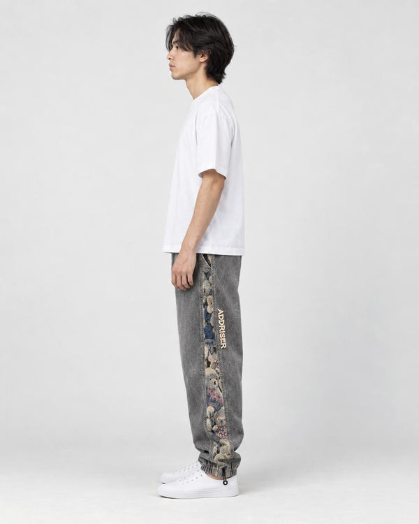 Model seen from the side in the washed gray denim joggers and white sneakers, showing the bear panel on the outer leg