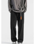 Black corduroy wide-leg pants with a black webbing belt and orange tag, worn with a gray sweatshirt and sneakers