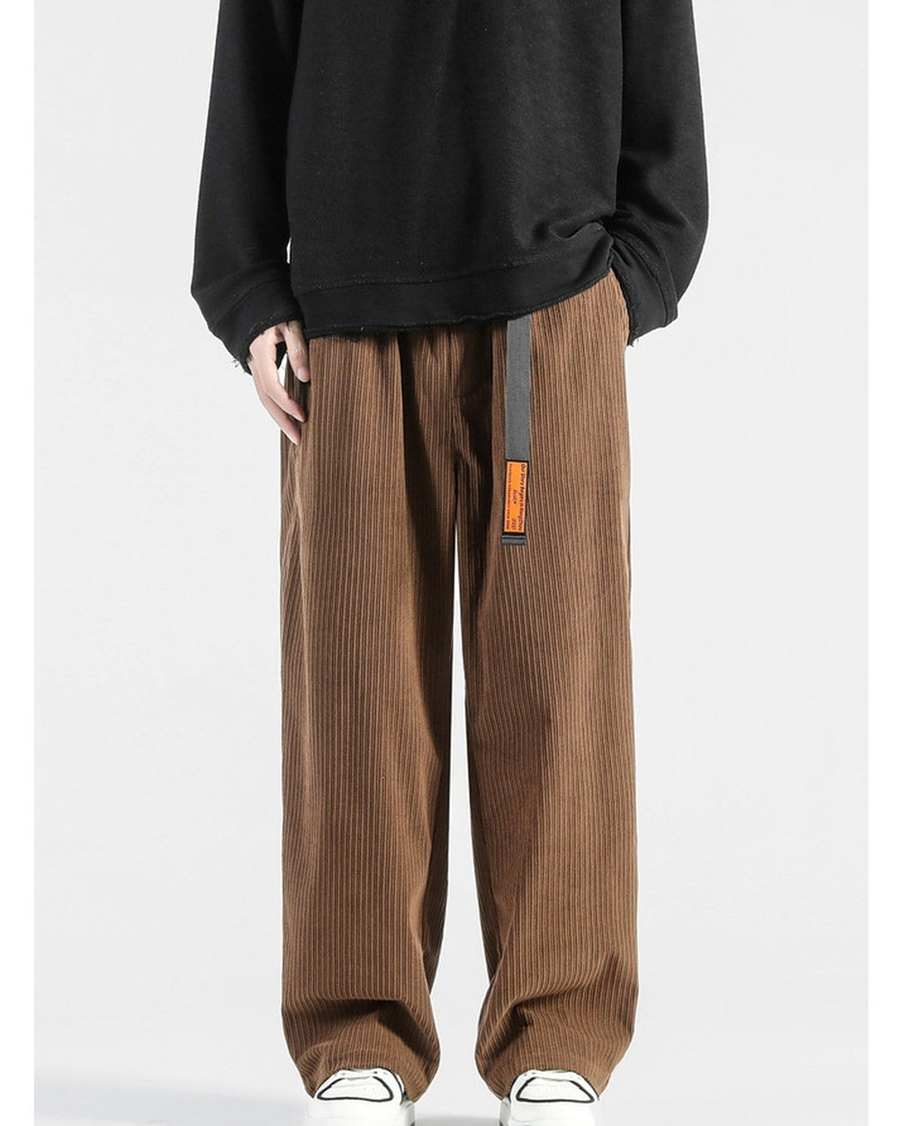 Brown corduroy wide-leg pants with a black webbing belt and orange tag, worn with a black sweatshirt and sneakers