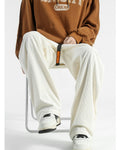 Man seated in the cream corduroy wide-leg pants, showing the roomy hip and the belt tail