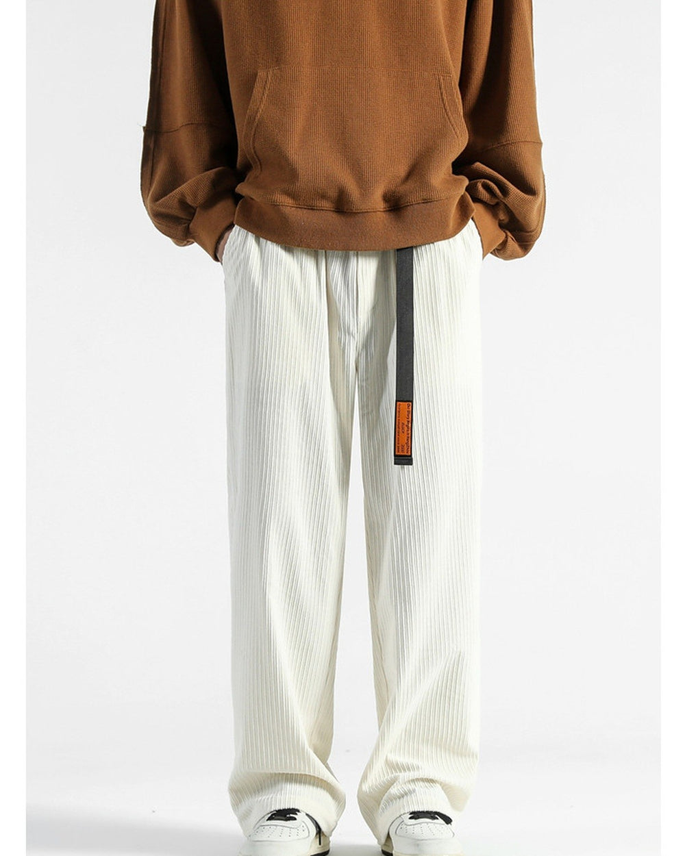 Cream corduroy wide-leg pants with a black webbing belt and orange tag, worn with a brown sweatshirt and sneakers
