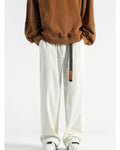 Cream corduroy wide-leg pants with a black webbing belt and orange tag, worn with a brown sweatshirt and sneakers