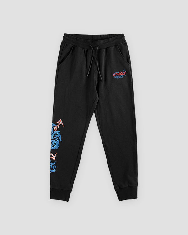 Black jogger pants laid flat with a red and blue logo on the thigh and a koi and wave on the lower leg