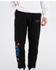 Man in black embroidered jogger pants with a white sweatshirt, front view with a hand in the pocket