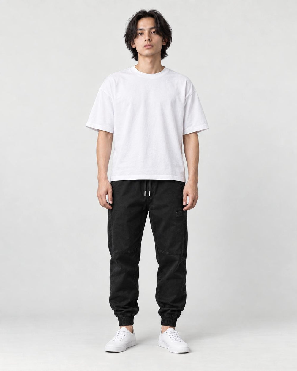 Man in black tapered jogger pants with ribbed cuffs, white tee and white sneakers, full length
