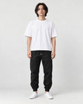 Man in black tapered jogger pants with ribbed cuffs, white tee and white sneakers, full length