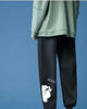 Black jogger sweatpants with a white cartoon bear and the word GOOD on the lower leg, rear three-quarter view