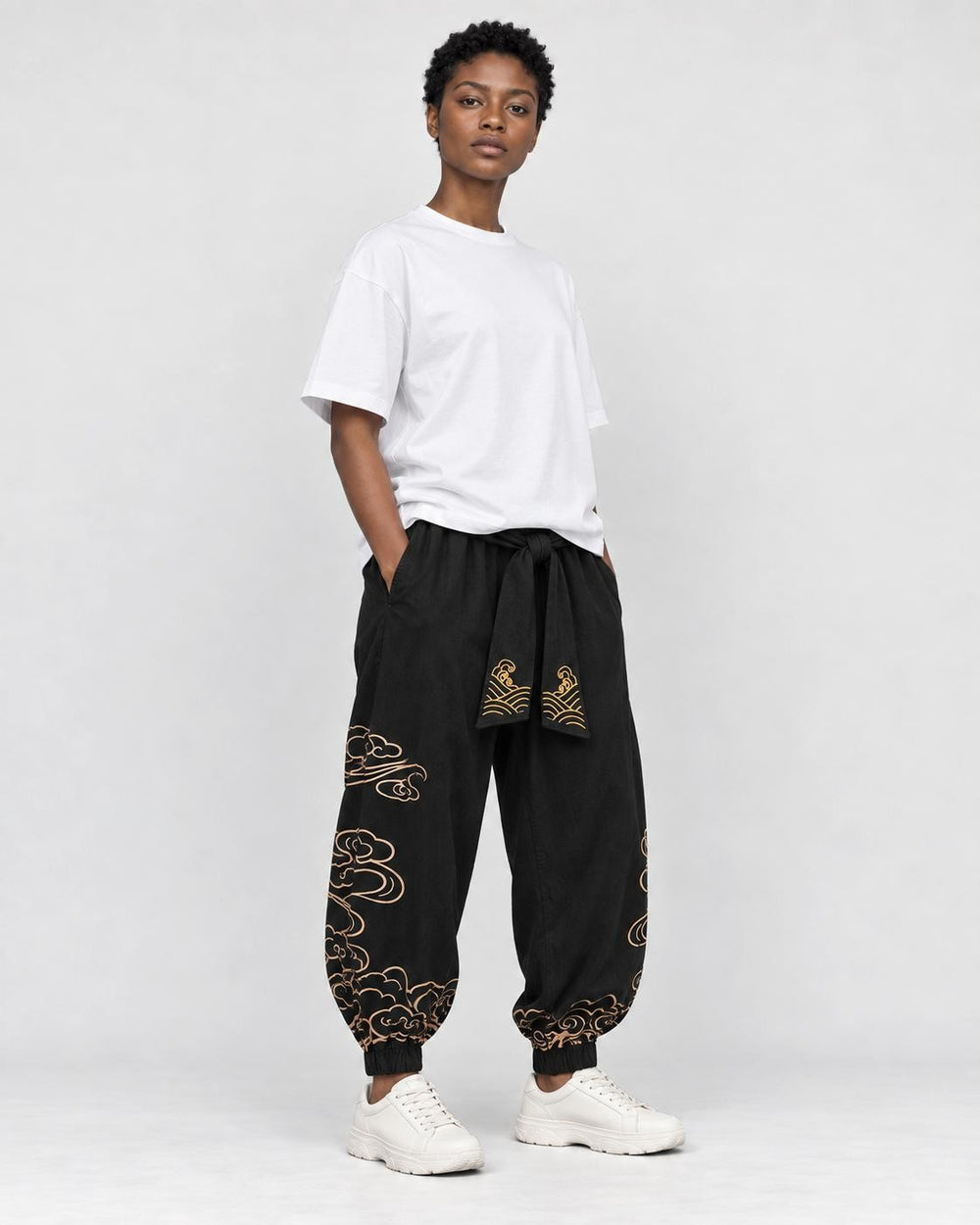 Model wearing the black cloud-embroidered lantern pants with a white tee and white sneakers, three-quarter view