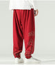 Red lantern pants with gold cloud embroidery on the lower legs and a knotted sash, worn with a white shirt