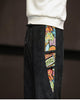 Close-up of the printed side panel with frog-button knots on the black corduroy joggers