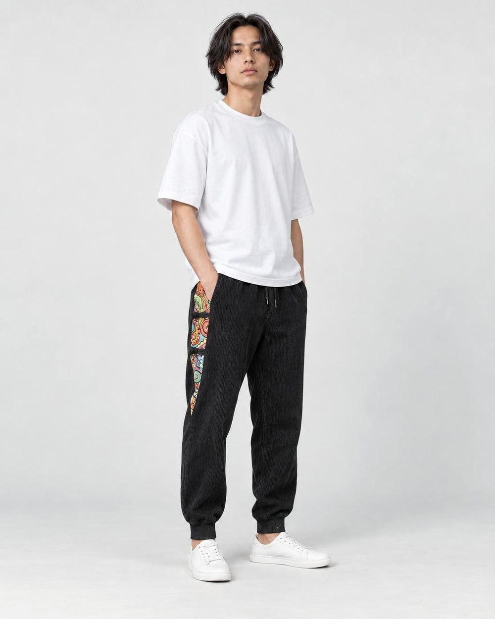 Model wearing the black corduroy joggers with printed side panels, a white tee and white sneakers, three-quarter view