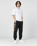 Model wearing the black corduroy joggers with printed side panels, a white tee and white sneakers, three-quarter view