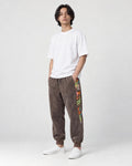 Model wearing the brown corduroy joggers with printed side panels, a white tee and white sneakers, three-quarter view