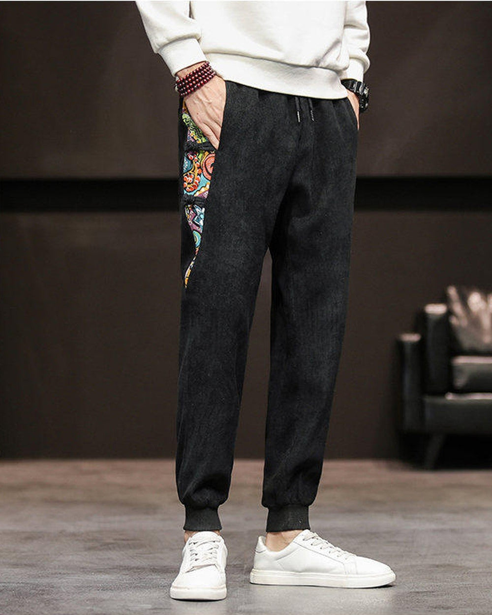 Black corduroy joggers with a printed side panel and ribbed cuffs, worn with a white sweatshirt and white sneakers