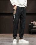 Black corduroy joggers with a printed side panel and ribbed cuffs, worn with a white sweatshirt and white sneakers